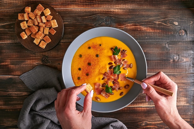 Dames handen houden crouton en lepel vast met traditionele pompoenpuree-roomsoep met worteluitjes