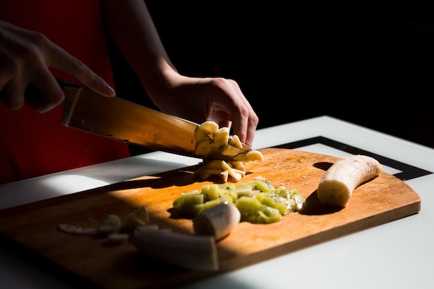 Dames handen snijden verse banaan op het houten bord in de keuken