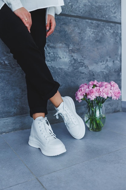 Damesbenen in zwarte broek en witte leren sneakers Moderne casual stijl Nieuwe schoenencollectie