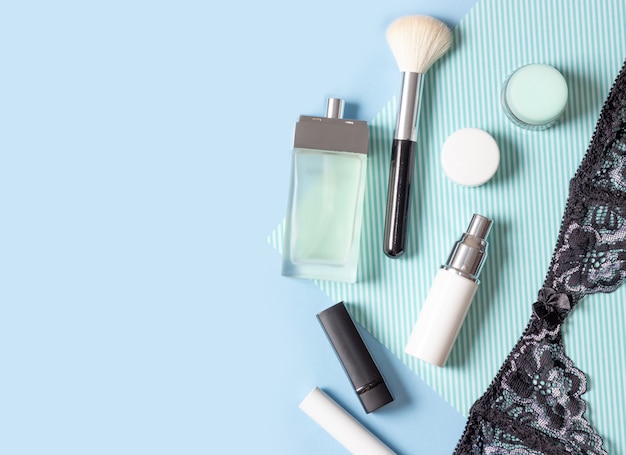 Damescosmetica en accessoires op een blauw gestreepte achtergrond: parfum, crème, lippenstift, make-upborstel. Mode en schoonheidsconcept.