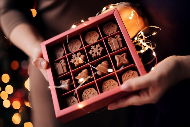 Foto dameshanden houden een prachtige kerstdoos met natuurlijke melkchocolade handgemaakt in de vorm van sneeuwvlokken