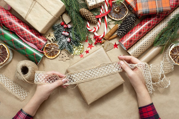 Dameshanden pakken en decoreren een kerstcadeau, de tafel is bedekt met beige kraftpapier en