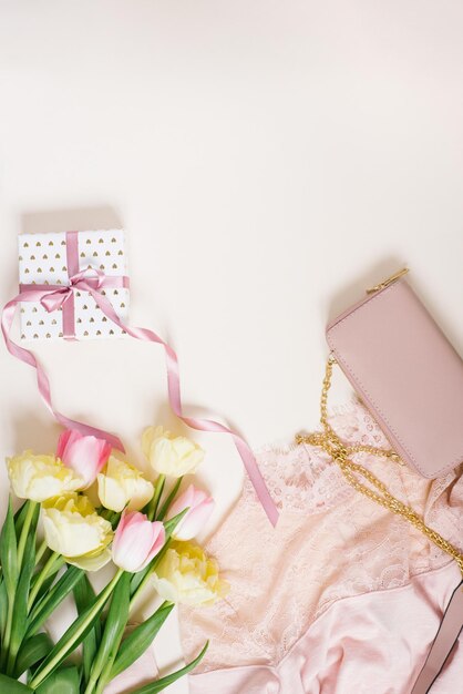 Dameskleding geschenkdoos tas en tulpenbloemen Minimalistische compositie in pastel beige en roze tinten Bovenaanzicht platte lay-out kopie ruimte Het concept van de verjaardag van een vrouw mode en bloggen