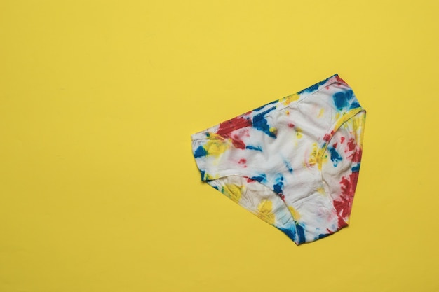 Damesslipjes zijn met de hand beschilderd in de stijl van tie dye op een felgele achtergrond. Gekleurd ondergoed in huis.