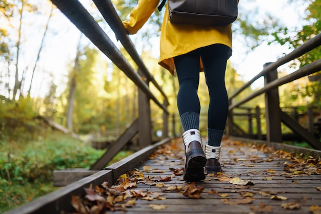 Damesvoeten in laarzen gaan langs een houten wandelpad in het herfstbos