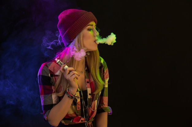 Dampend meisje. Jonge hipster vrouw vape e-sigaret op zwarte achtergrond. Hiphop-stijl. Damp-concept. E-sigaret vapen. Studio opname