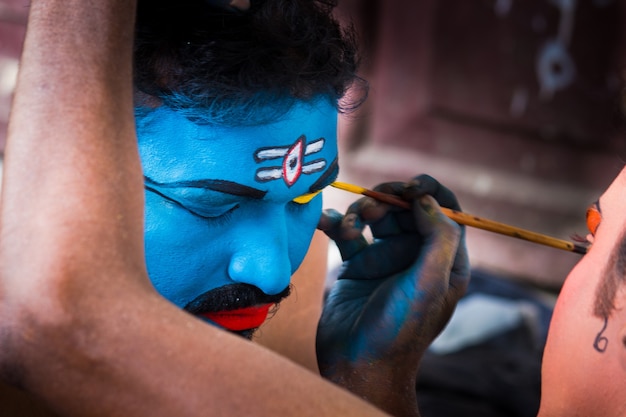 Танцевальный артист делает макияж перед выступлением на сцене во время индийского фестиваля.