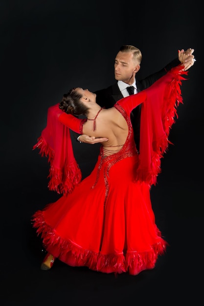赤いドレスのダンスボールルームのカップルは、黒の背景に分離されたダンスポーズ。ワルツ、タンゴ、スローフォックス、クイックステップを踊る官能的なプロのダンサー。