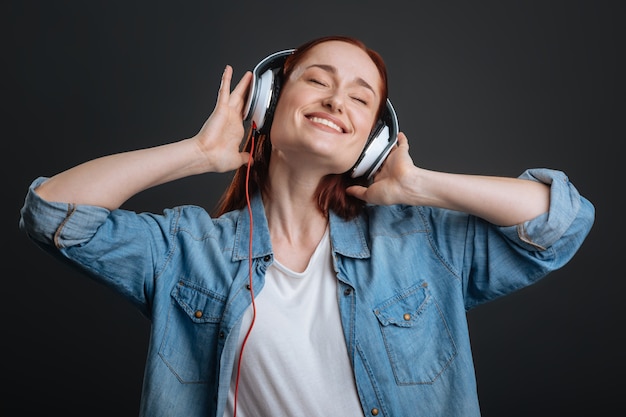 Dance to the sound. Talented artistic gorgeous lady putting the headphones on for enjoying a new song and closing her eyes with pleasure