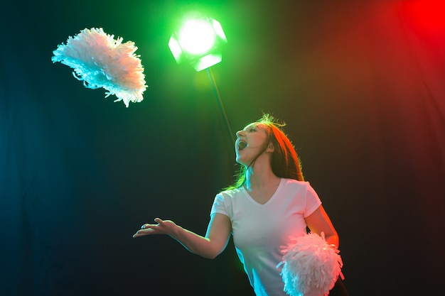 Dance, sport and people concept - pretty young woman dancing in darkness with pompoms and smiling.
