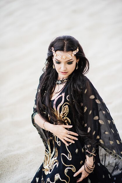Dancer bellydance and Khaleegy (Khaliji) in a black suit in the desert against the background of sand. 