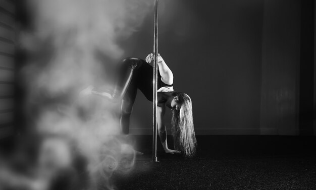 The dancer on the pylon in the studio. Girl doing exercises on a sports equipment.