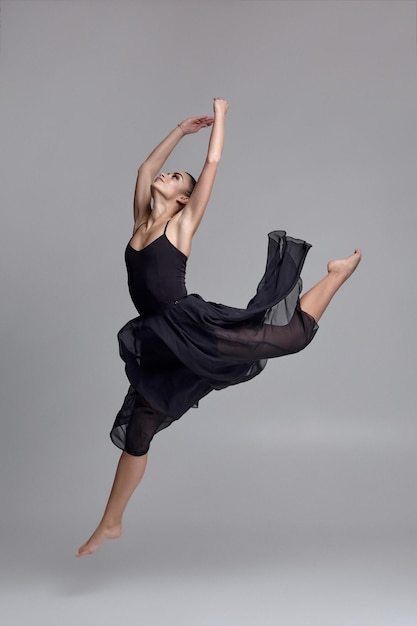 Dancing ballerina in a black dress. Contemporary graceful performance on a gray background.