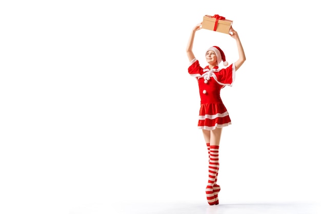 Dancing ballerina with a box of gifts in her hands on pointe shoes in Santa Claus costume isolated on white background