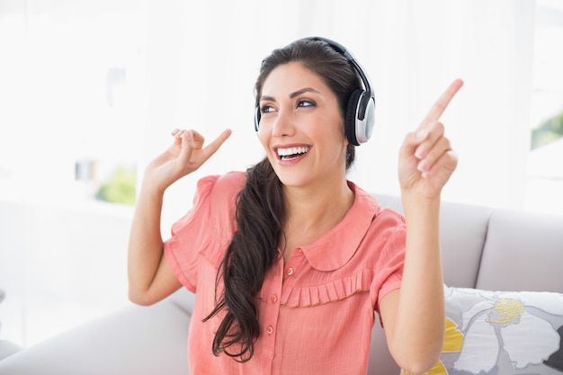 Dancing brunette sitting on her sofa listening to music