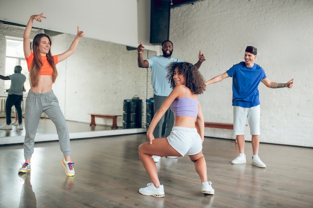 Танцы. Группа энергичных веселых молодых людей в спортивной одежде и тренера в танцевальном зале с большим зеркалом