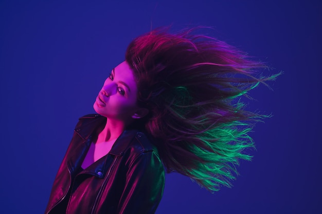 Dancing, hairs flying. Caucasian woman's portrait isolated on blue studio background in neon light. Beautiful female model. Concept of human emotions, facial expression, sales, ad. Trendy colors.