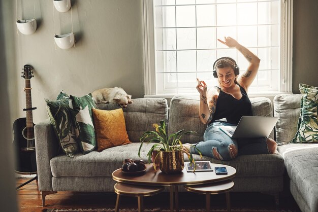 Photo dancing headphones and woman on sofa and laptop happy energy and mental health music in her home young person on couch listening to audio tech electronics and podcast on computer in living room