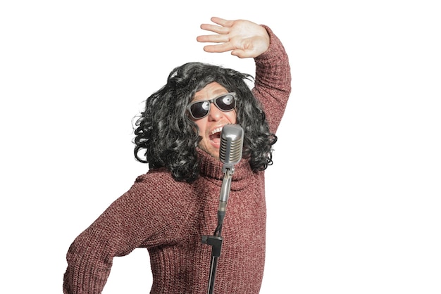 Танцующий мужчина в парике, свитере и солнцезащитных очках у микрофона изолирован