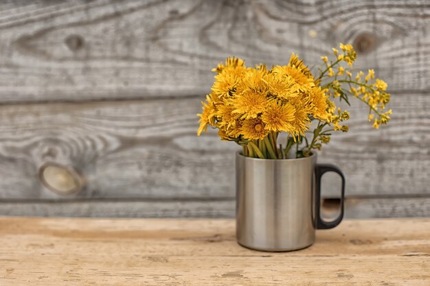 Dandelion bouquet in a metal mug. Wood background. copy space