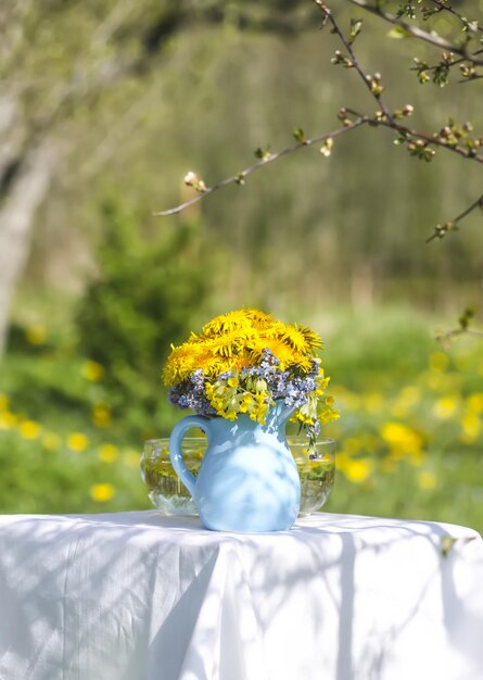 日光の下で青いセラミック水差しのタンポポの花屋外の花の組成