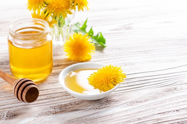 Dandelion honey in a jar and fresh flowers on white wooden table. copy space