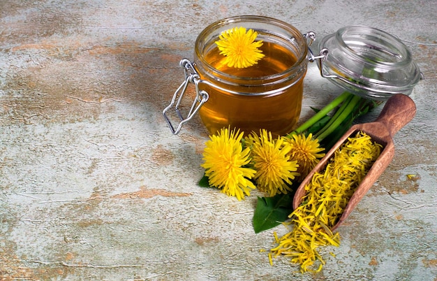 Dandelion jam in glass jar, flowers and petals of dandelions on textured background. Free space for your text.