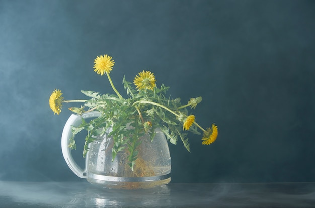 Photo dandelion with roots and leaves in a glass teapot