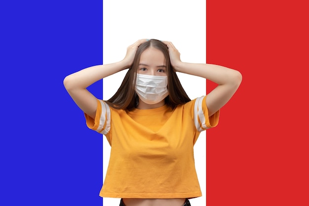 Danger and panic due to coronavirus in France Young girl in antibacterial medical mask holds her head scared on the background of the flag