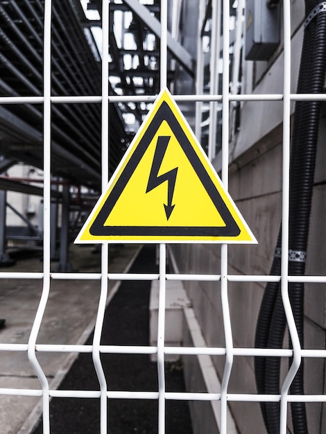 Photo danger sign high voltage in a yellow triangle on a metal grid
