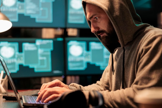 Dangerous hacker trying to break database server, using virus
to code malware and steal big data at night. working with multiple
monitors and hacking information system, wearing hood.