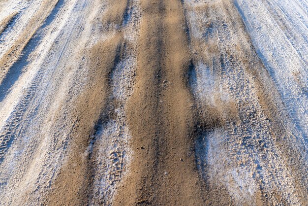 冬の危険な道路、降雪後の冬の車の痕跡がある滑りやすい泥だらけの道路、