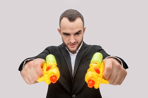 Photo dangerous young man in suit hold two water pistols in hands and direct them straight. he is angry and serious.