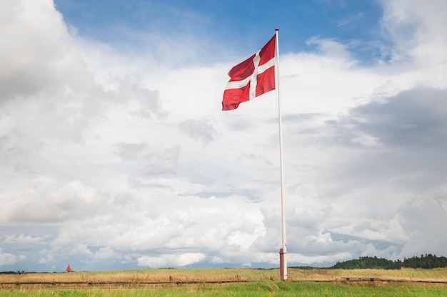 Датский флаг на флагштоке на фоне красивого облачного неба