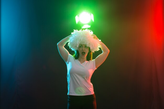 Dansen, cheerleaden en mensenconcept - jong meisje in duisternis onder kleurrijk licht met pompons op haar hoofd.