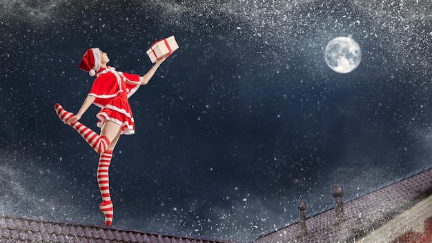 Dansende meisjesballerina met een cadeau in haar handen in een kerstmankostuum op het dak van een huis op kerstnacht tegen de achtergrond van de sterrenhemel