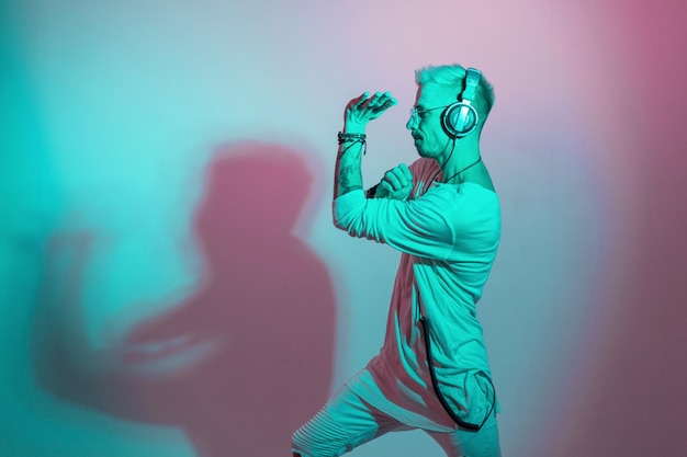 Dansers man met bril en koptelefoon in witte kleren luisteren naar muziek en dansen in de studio met roze en blauwe kleur