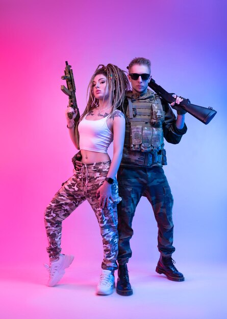 사진 자동 소총을 가진 대담한 세련된 소녀와 네오에서 에어소프트 총을 가진 군복을 입은 남자
