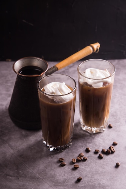 On a dark background a coffee maker and glasses with cold iced coffee and whipped cream