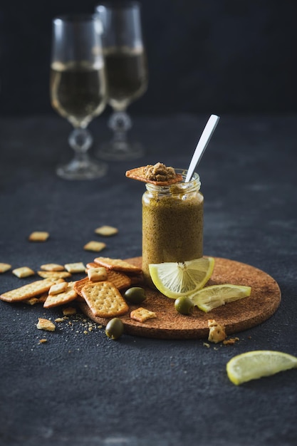 On dark background olive pesto in jar with crackers