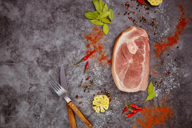 On dark background raw pork chops are arranged with spices and a fork