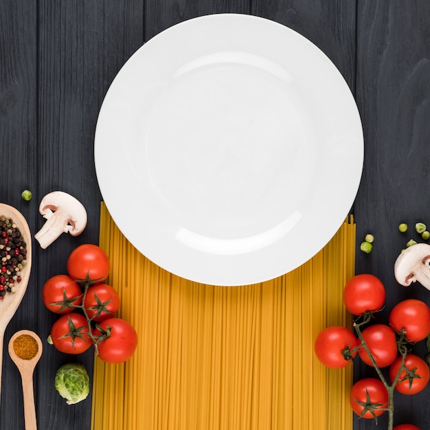 Foto su uno sfondo scuro si trova un piatto, pasta, pomodori, spezie