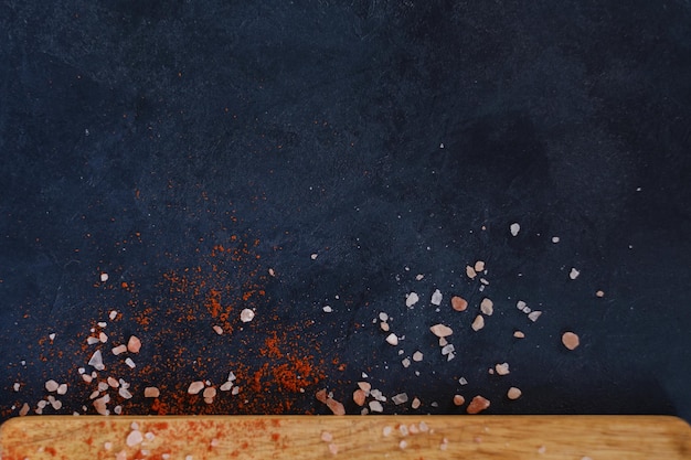 Dark background with scattered chunks of salt and red pepper or paprika spice condiments rough textured surface food preparing and cooking concept