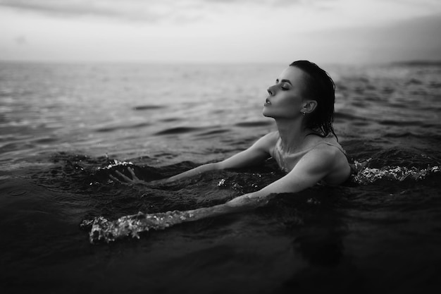 Foto ritratto in bianco e nero scuro di una ragazza gentile sensuale nell'acqua prima del tramonto in estate.