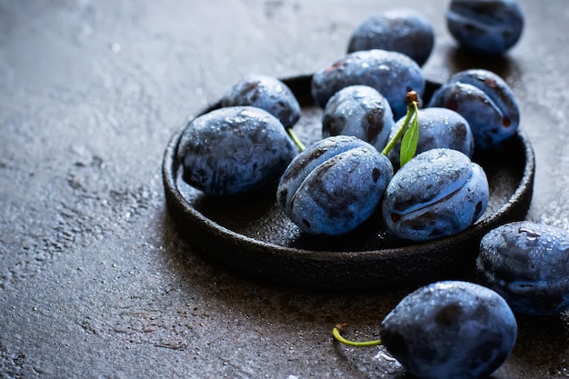 Dark blue plums in cast iron plate on black background closeup