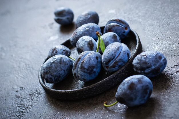 Dark blue plums in cast iron plate on black background closeup