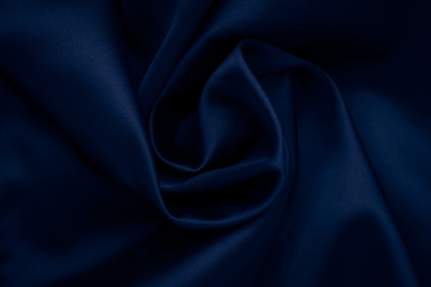 Dark blue wavy silk background. Abstract surface of fabric, textile of cloth. Wallpaper of satin, crumpled texture of material.