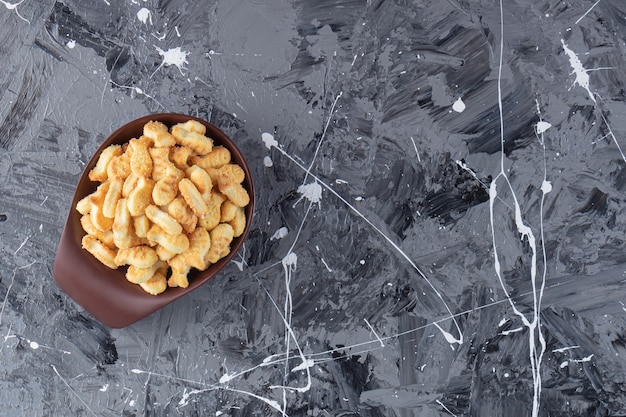 Dark bowl of tasty salted crackers on marble table. 