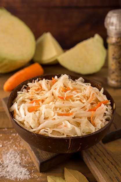 Dark bowl with sour sauerkraut on cutting board on wooden brown background close up and ingredients