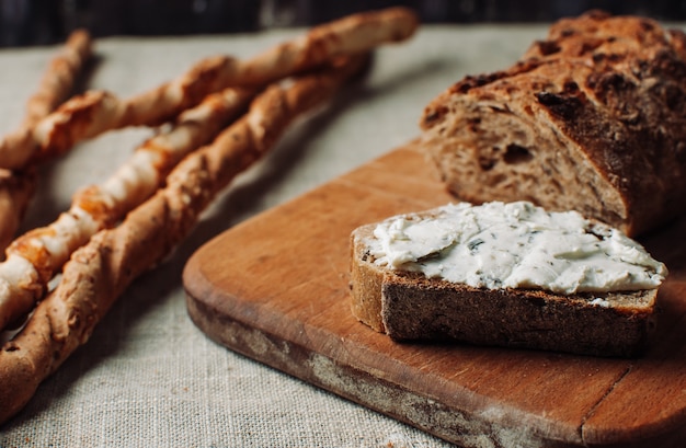 暗いパンは、木の板にカットしたハーブとカッテージチーズで広がっています